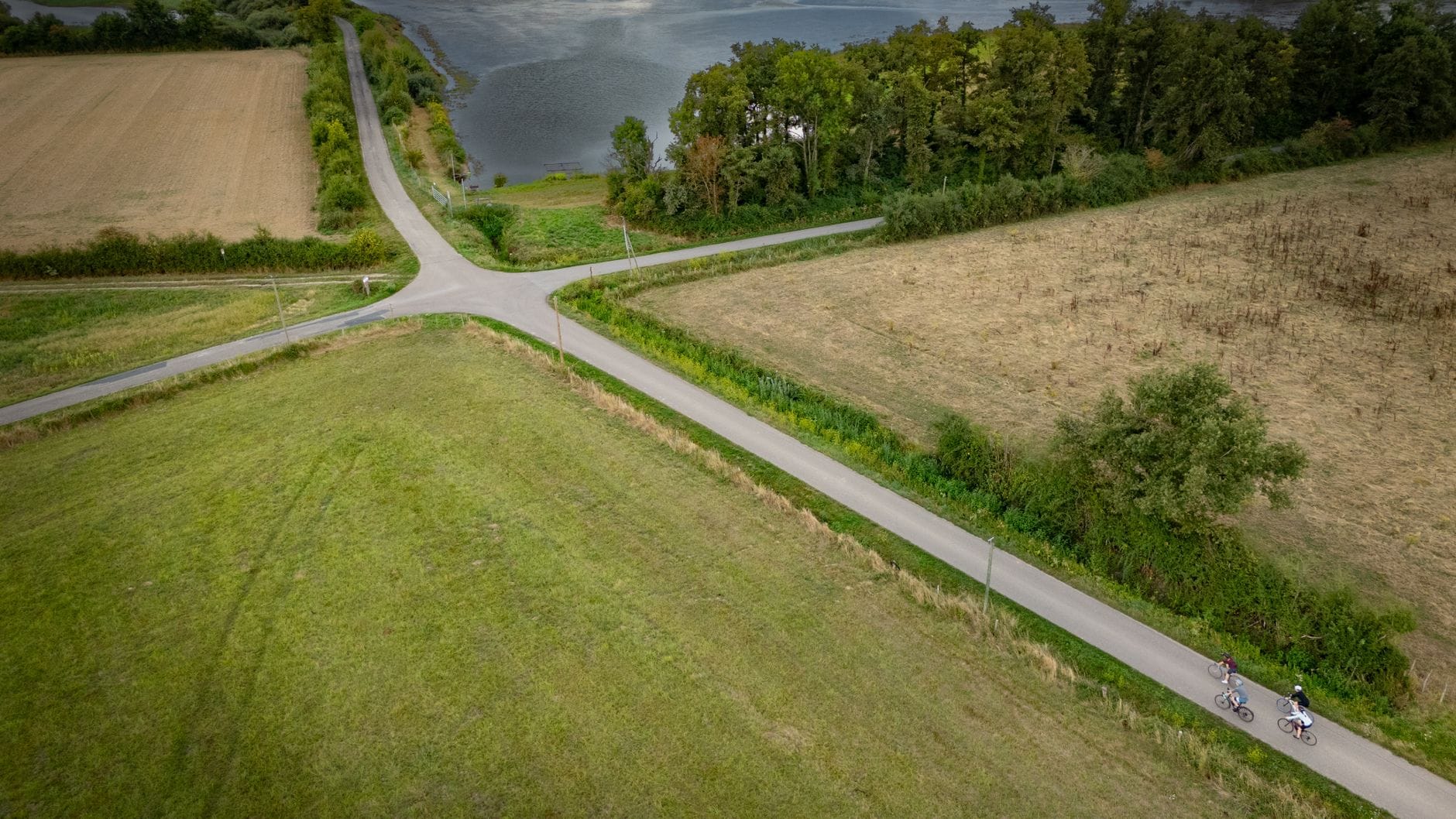 Rowerzyści na wiejskiej drodze obok jeziora i pól nad Jeziorem Bytyńskim